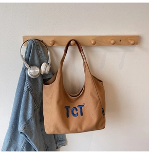 Gros plan du sac fourre-tout en toile marron avec broderie TCT et anses en cuir