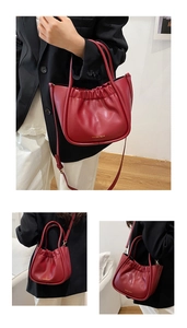 Detailansicht der tiefroten Plissee-Ledertasche mit Goldlogo und Schultergurt