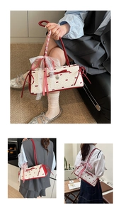 Detail of white baguette bag with red bow prints and lace ribbon featuring heart pendant