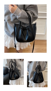 Detail der schwarzen Plissee-Handtasche mit goldenem Logo und verstellbarem Schultergurt