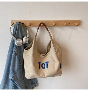 Gros plan sur un cabas en toile beige avec broderie TCT et anses en cuir marron foncé