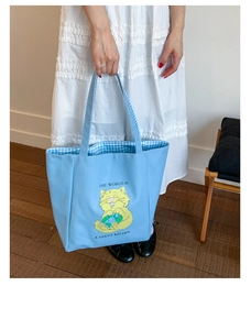 Detail of light blue canvas tote bag showing the cartoon cat print and inner checkered lining
