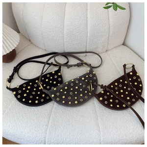 Three studded crescent shoulder bags in black, grey, and brown on soft white fabric