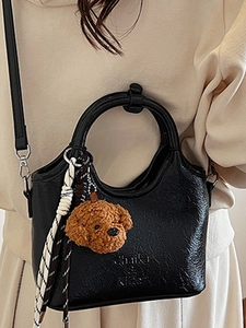 Fashionable black bucket tote bag with leather texture and poodle charm on a model