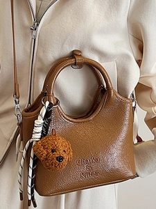 Brown vintage faux leather tote bag with round handle and teddy bear charm on cream background