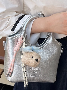 Fashionable silver metallic bucket tote bag with plush charm shown being held by a model