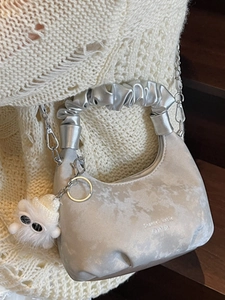 Silver pleated cloud bag with metallic chain strap and plush monster pendant on knit backdrop