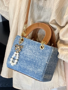 Blue denim crossbody bag with brown leather handles and pearl butterfly pendant