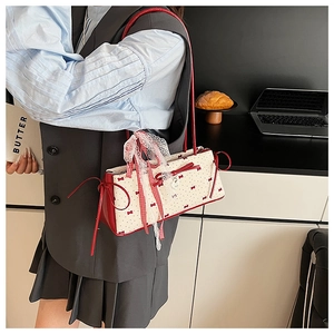 Detail of cream shoulder bag with red bow prints and lace ribbons on a model's arm