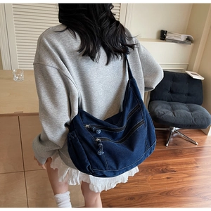Detail of blue denim hobo bag featuring multiple zip pockets and adjustable wide strap