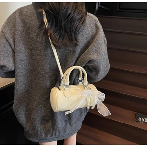 Detail of beige Boston bag with lace bow and pearl pendant worn over gray sweater