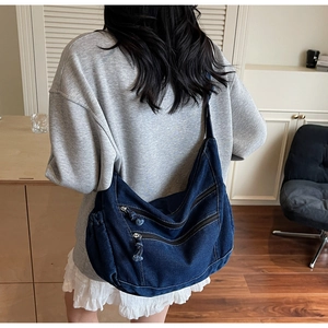 Detail shot of a dark blue large denim hobo bag featuring multiple zip pockets