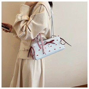 Detailed view of light blue shoulder bag with red bows and lace trim on a model
