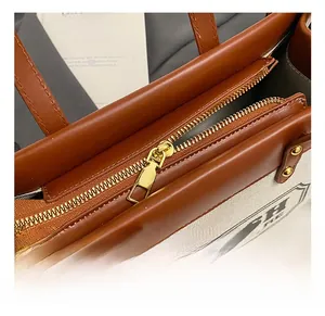 Detail von goldenem Reißverschluss und braunem Lederbesatz auf beiger Canvas-Tasche
