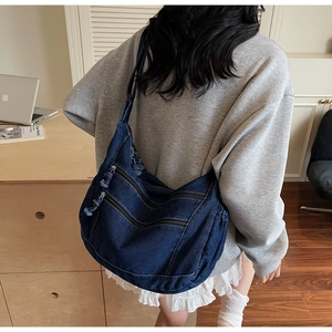 Detail of blue denim crossbody bag with multi-layer zippers and woven pulls in lifestyle setting