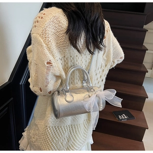 Detail view of silver cylindrical handbag with pearl charm and lace bow on wooden stairs