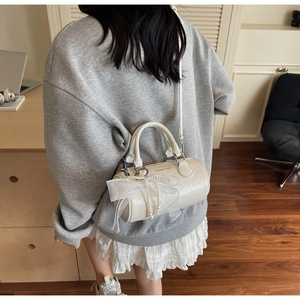 Detail of cream barrel bag with lace bow and pearl charm worn over the shoulder