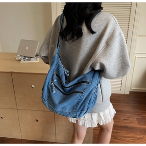 Detail of blue denim crossbody bag featuring multiple horizontal zippers and wide shoulder strap