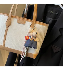 Close-up of beige woven tote bag with leather trim and a cute plush bear charm