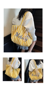 Détail du sac cabas en toile à rayures jaunes, texte Melody et nœud en dentelle blanche