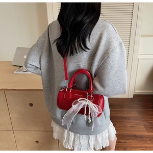 Detail of red cylindrical bag featuring white lace bow and faux pearl charms for women