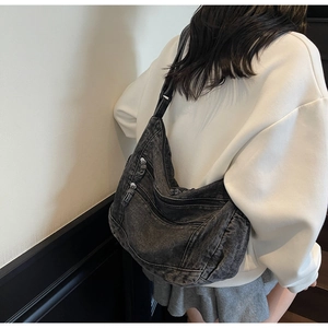 Detail of grey denim crescent crossbody bag with multiple zip pockets and adjustable strap