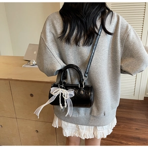 Detail of black glossy leather Boston bag with white lace bow and pearl charm