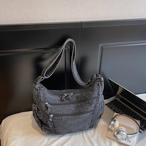 Detail of charcoal grey washed denim crossbody bag featuring three zipper pockets on front