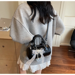 Detail of black cylinder bag with lace bow and pearl pendant shown in lifestyle setting