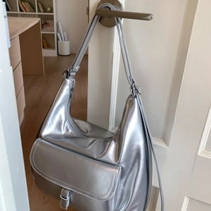 Detail of a metallic silver hobo bag with front pocket hanging on a white door handle