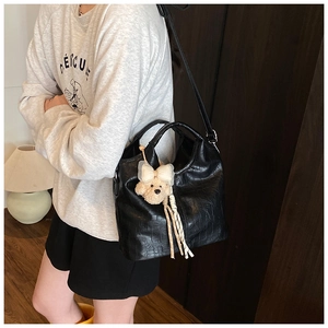 Dettaglio di una grande borsa tote in pelle nera con ciondolo a orsetto indossata da modella