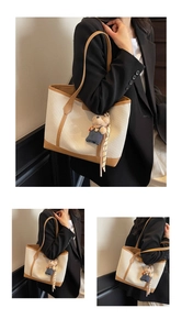 Detail of cream canvas tote bag with brown leather trim and a cute teddy bear charm