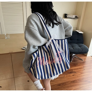Détail du sac cabas en toile rayée bleue avec broderie rose et nœud en dentelle