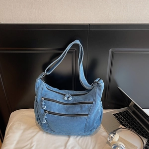 Detail of blue denim crossbody bag featuring three functional parallel front zippers