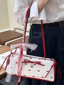 Sweet white shoulder bag with red bow patterns and polka dots held by a model