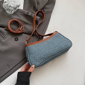 Dettaglio della borsa denim blu con borchie argentate e finiture in pelle marrone su blazer