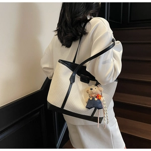 Detail of a large woven tote bag with black trim and a cute plush bear charm on a model