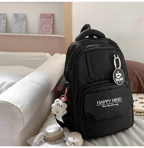 Detail of black school backpack featuring HAPPY MIND print and cute teddy bear pendant