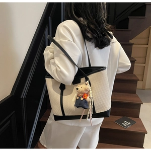 Detail of large beige and black tote bag with cute bear charm on model shoulder