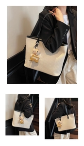Detail of beige woven tote bag with black trim and a cute plush bear charm accessory