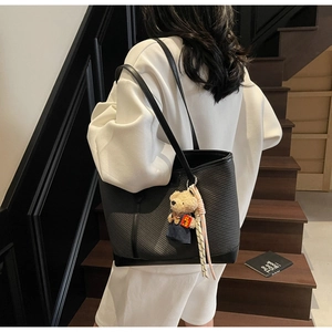 Rear view of black tote bag with woven texture and bear pendant on a model