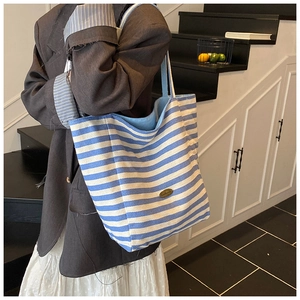Détail du sac cabas en toile rayé bleu et blanc avec logo sur une bandoulière élégante