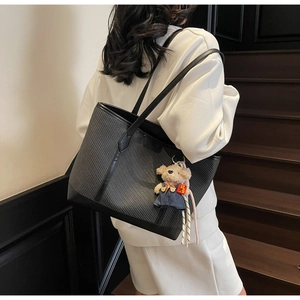 Macro detail of black woven leather tote bag with cute plush bear charm on strap