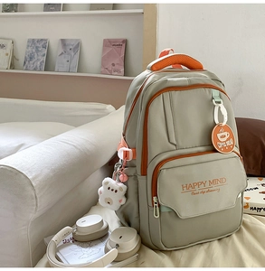 Detail view of green nylon backpack showing orange zipper accents and plush bear pendant