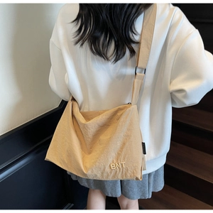 Rear view of a beige nylon messenger bag with BNT embroidery on a model walking on stairs