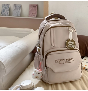 Detail of cream school backpack with Happy Mind print, plush bear and coffee charm