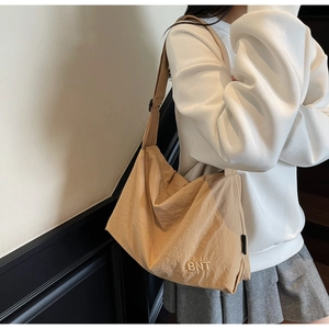 Detailed close-up of beige nylon crossbody bag with BNT embroidery on the corner