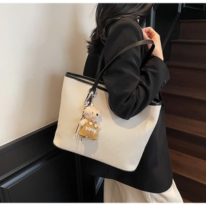 Détail d'un sac cabas tissé crème avec anses noires et charmant pendentif d'ours