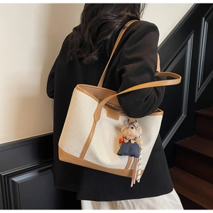 Detail of woven texture tote bag with brown leather trim and cute plush bear charm