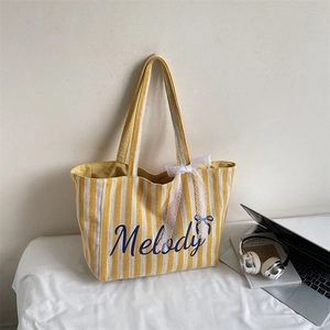 Détail du sac cabas en toile rayé jaune avec lettrage Melody et décoration de nœud en dentelle